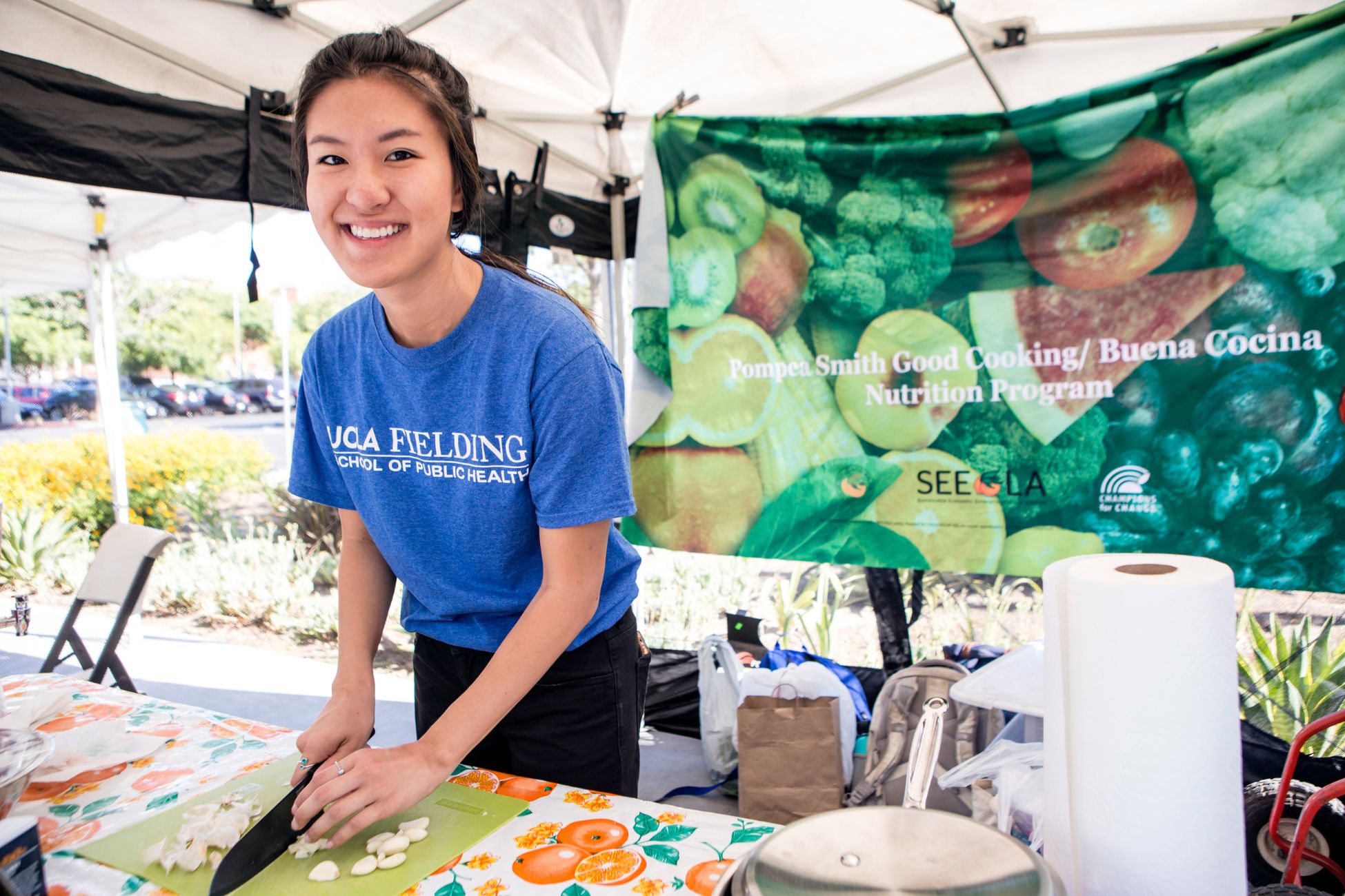 Young Asian American woman smiles at the camera as she chops food at a nutrition information booth